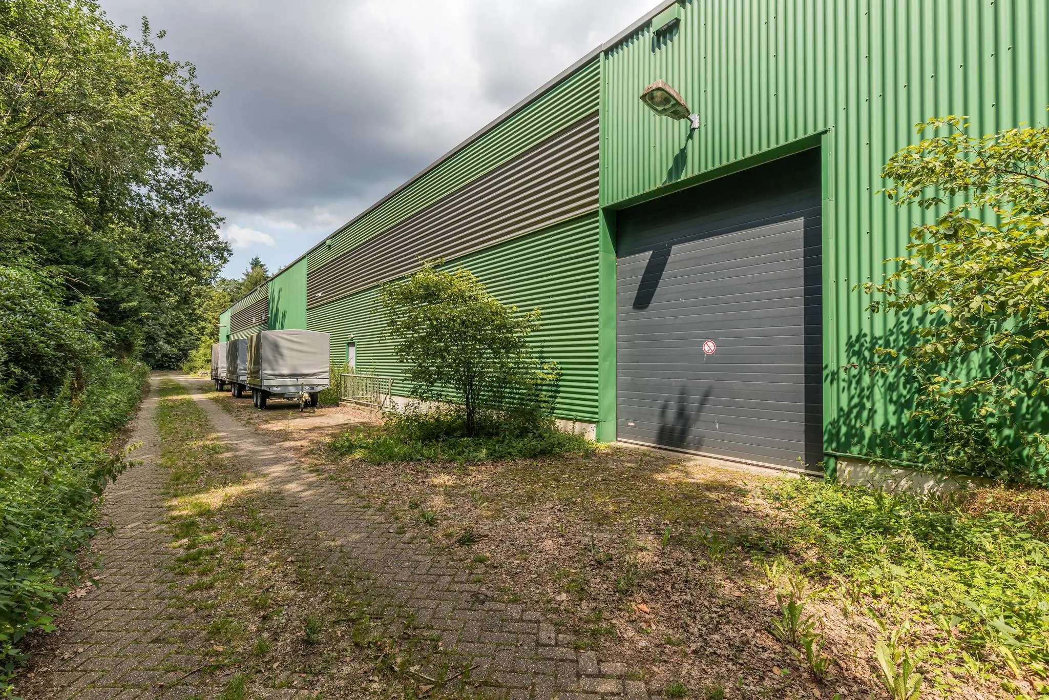Groen industriepand aan de Laan Blussé van Oud-Alblas met geparkeerde aanhangers en omliggend groen.